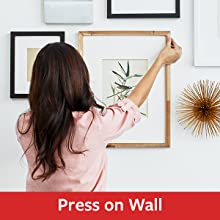 Woman pressing a frame to a wall with Command Picture hanging strips