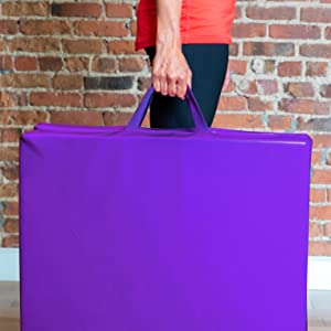 Female holding a folded purple mat with handles with a brick wall background