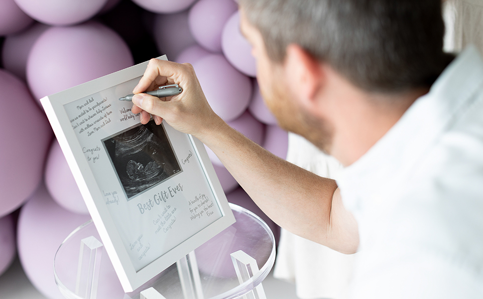 Family member signing baby sonogram guestbook frame at baby shower